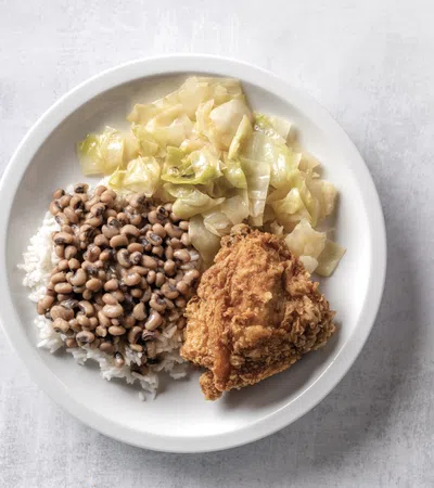 Plate with fried chicken, cooked cabbage, and black-eyed peas over white rice on a light background.