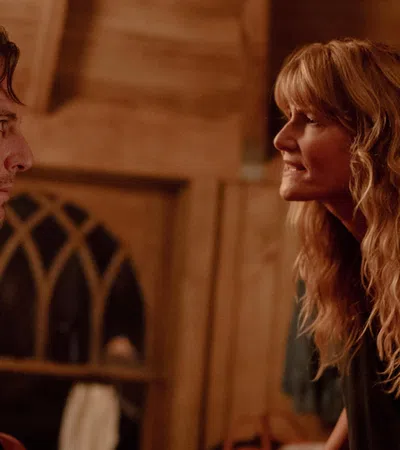 Man and woman engage in an intense conversation inside a warmly lit wooden cabin at night.