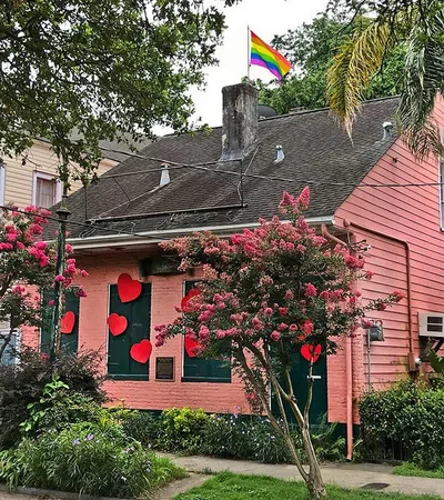 Pink house decorated with red hearts on windows and a rainbow pride flag flying on the rooftop.