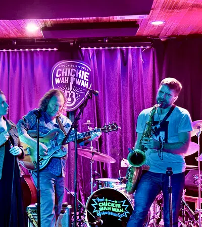 Live band performing with guitar, saxophone, vocals, and keyboard on stage at Chickie Wah Wah venue.