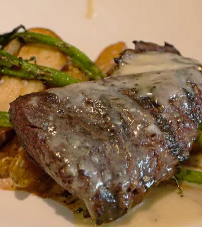 Grilled steak with creamy sauce served with roasted potatoes and asparagus on a white plate.