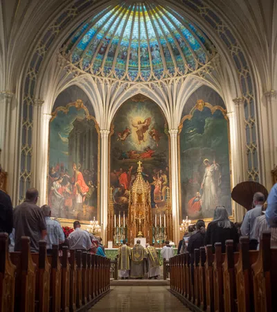 Congregation attending mass in a decorated Catholic church with stained glass dome and religious paintings