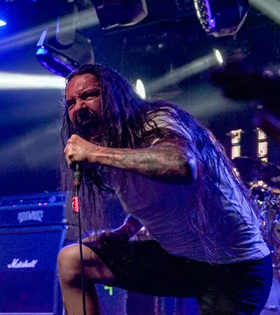 a man with long hair holding a microphone in front of a drum set