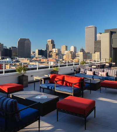 Stylish rooftop lounge with city skyline view and modern furnishings under a clear blue sky.