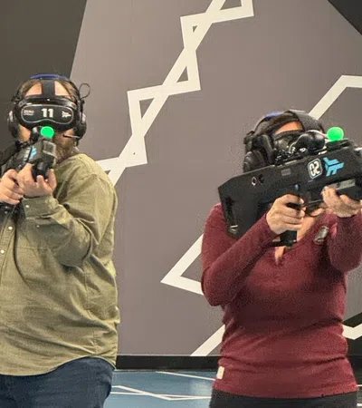 Two people wearing VR headsets and holding controllers in a modern room with geometric wall and floor designs.