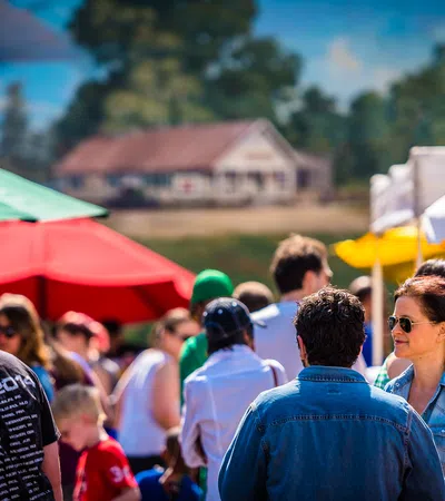 People socializing outdoors at a colorful market with red, green, and yellow umbrellas on a sunny day.
