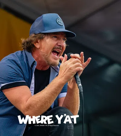 Male singer passionately performing on stage wearing a blue cap and shirt, holding a microphone.