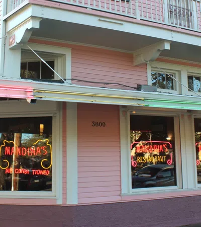 Pink corner building with neon signs reading Mandina's restaurant and outdoor benches on the sidewalk