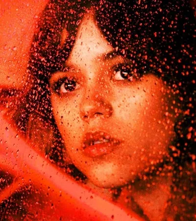 Young woman looking through a rain-streaked window with warm red ambient lighting
