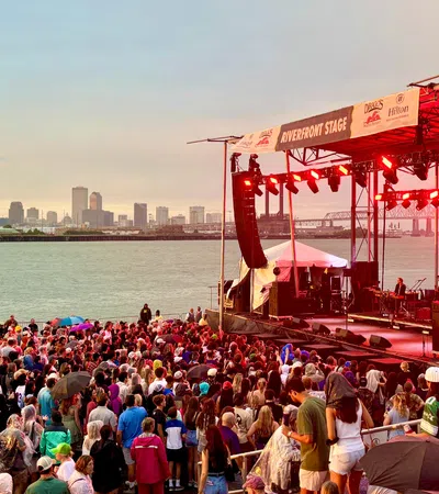 Crowd enjoying live music at the Riverfront Stage with city skyline and river in the background at sunset.