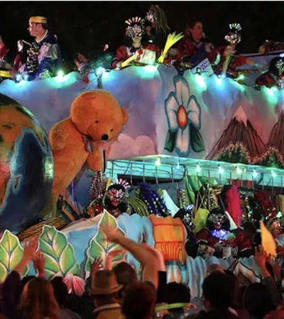 Colorful parade float with large globe, teddy bear, flowers, and people celebrating at night with lights.
