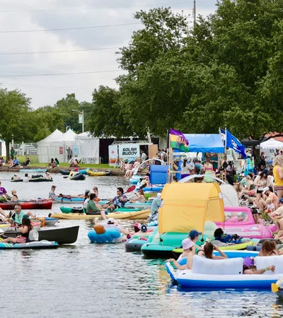 Crowd enjoying a summer festival by the water with kayaks and colorful inflatables.