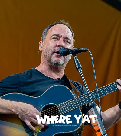Musician performing on stage, playing an acoustic guitar with a microphone.