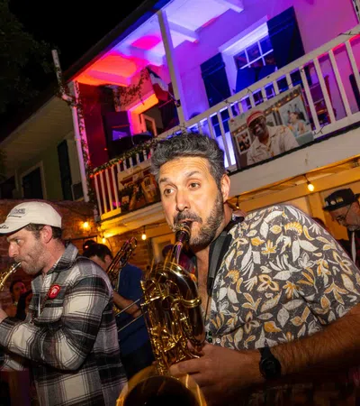 Musicians passionately playing saxophones at a lively outdoor night event with colorful lighting and a crowd.