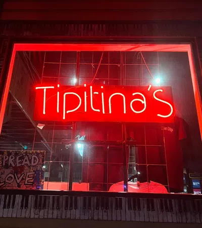 Red neon sign displaying Tipitina's in a window with a Spread Love sign nearby at night.