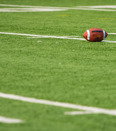 American football resting on green turf near white yard lines on a sunny day at the stadium
