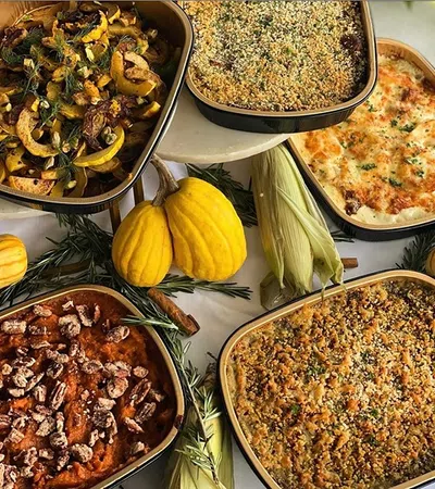 Assorted baked autumn dishes with squash, corn, pecans, and herbs arranged on a white tablecloth