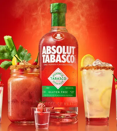Absolut Tabasco vodka bottle surrounded by four spicy cocktails with garnishes on a red background.