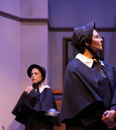 Three actors in period costumes engage in a dramatic scene on stage with serious expressions and historical attire.