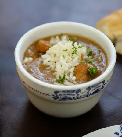 Bowl of gumbo topped with rice and parsley, served with bread on a dark surface.