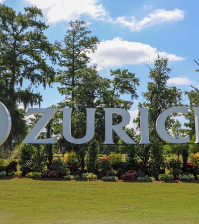 Zurich company sign in a landscaped setting with trees and flowers under a blue sky.