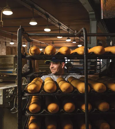 a person in a hat behind a shelf of breads
