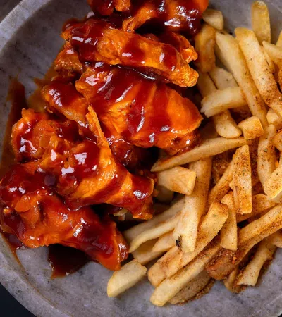 Plate of barbecue chicken wings and seasoned French fries on a gray dish with dark background.