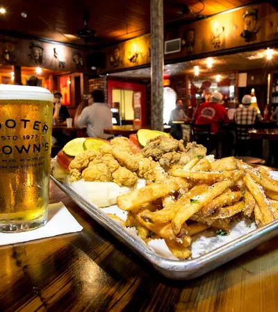 Tray of fried seafood, fries, and pickles with a cold beer in a cozy bar setting at Cooter Brown's.