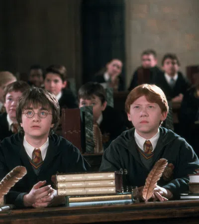 a couple of boys sitting at a table with books and Rupert Grint et al. in the background