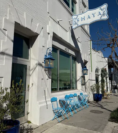 Charming exterior of Shaya restaurant with blue chairs, lanterns, and bright white walls under a clear blue sky.