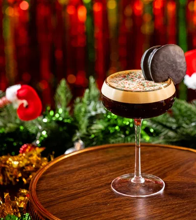 Festive holiday cocktail with creamy foam and chocolate garnish on wooden surface with Christmas decorations.