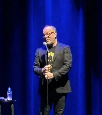 a man standing at a podium with a microphone and a blue curtain