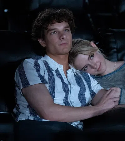 Young couple sitting closely in a dark movie theater, woman resting her head on man's shoulder holding hands.