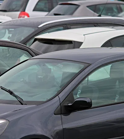 Close-up of multiple parked cars in a crowded parking lot on a cloudy day with raindrops visible on windows.