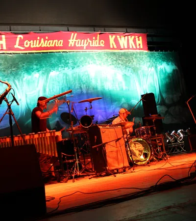 Live band performing on stage under KWKH Louisiana Hayride banner with saxophone, drums, and guitar.
