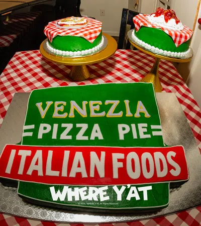 Colorful Italian-themed cake with 'Venezia Pizza Pie' and side cakes on a checkered tablecloth.