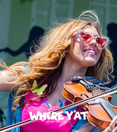 Woman with sunglasses playing violin joyfully at a vibrant outdoor music festival.