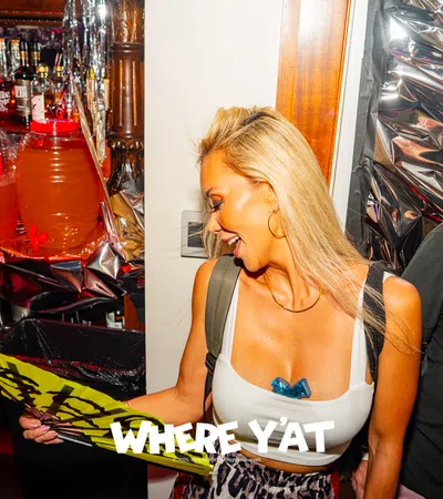 Woman in white tank top holding a yellow fan at a lively party bar with drinks and decorations at Tales of the cocktails.