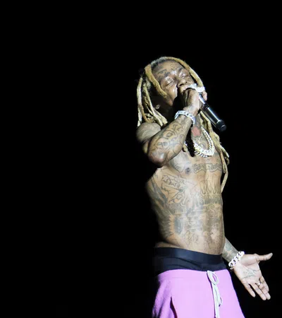 A tattooed rapper performs passionately on stage with a microphone, spotlighted against a dark background.
