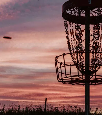 Silhouette of person throwing disc towards disc golf basket at sunset with colorful sky