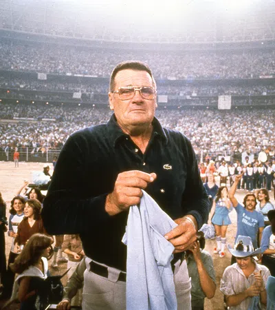 Man in glasses holding a towel at a crowded stadium event with cheering fans in the background