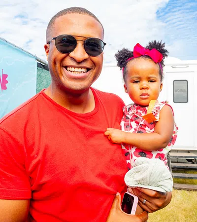 Smiling man in sunglasses holding toddler girl with bow at outdoor fried chicken festival under blue sky
