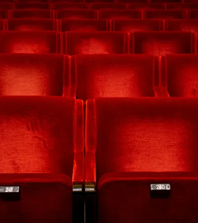 Empty red velvet theater or cinema seats arranged in rows with seat numbers visible on each seat.