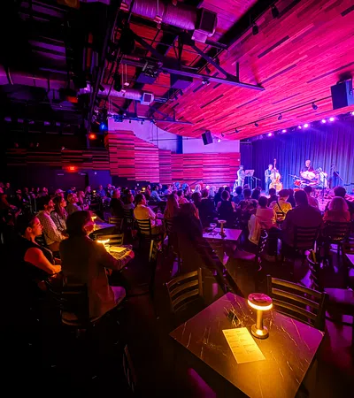 Audience enjoying live jazz performance in dimly lit intimate club with warm wooden decor and purple stage lighting