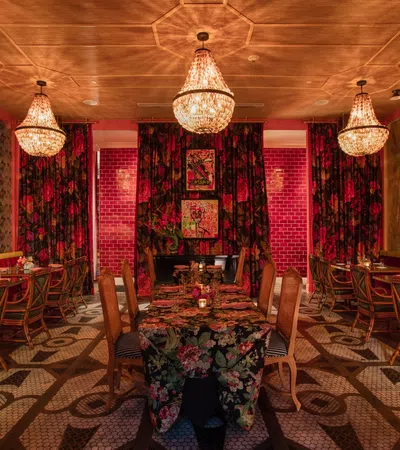Elegant restaurant interior with floral patterns, crystal chandeliers, wooden chairs, and a warm, cozy atmosphere.