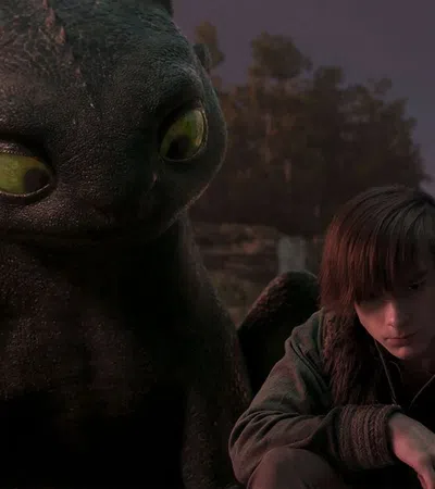 Young boy sitting beside a large black dragon with green eyes during dusk in a forest setting.