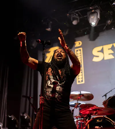 a person holding a microphone and standing in front of a drum set