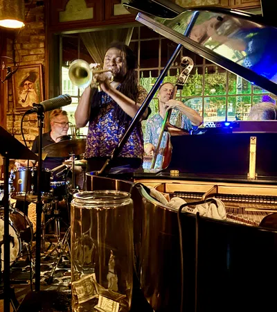 Jazz band performing live with trumpet, drums, double bass, and grand piano in cozy indoor venue.