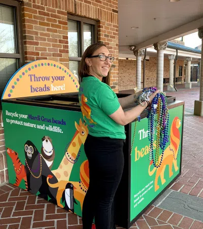 Woman recycling colorful Mardi Gras beads at a decorated collection bin to protect wildlife and nature.