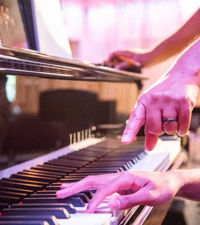 Person playing piano while another hands points at specific piano keys during a lesson.